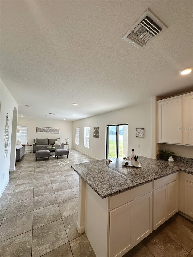 kitchen with white cabinetry, dark stone countertops, a textured ceiling, and kitchen peninsula