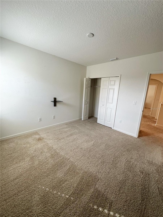 unfurnished bedroom featuring a textured ceiling, carpet floors, and a closet