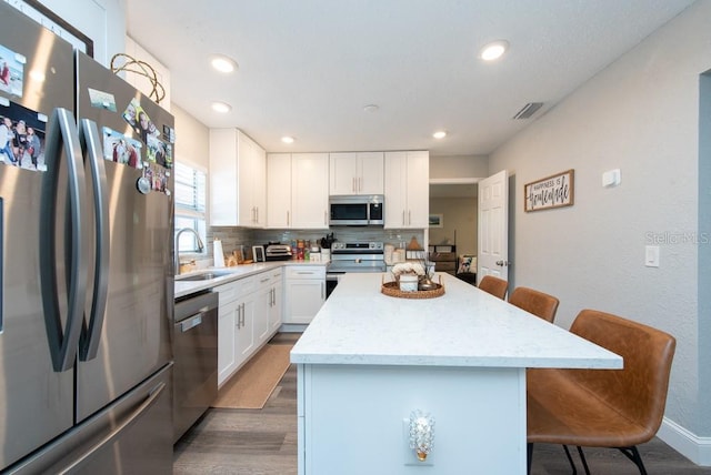 kitchen with appliances with stainless steel finishes, white cabinetry, sink, and a kitchen island