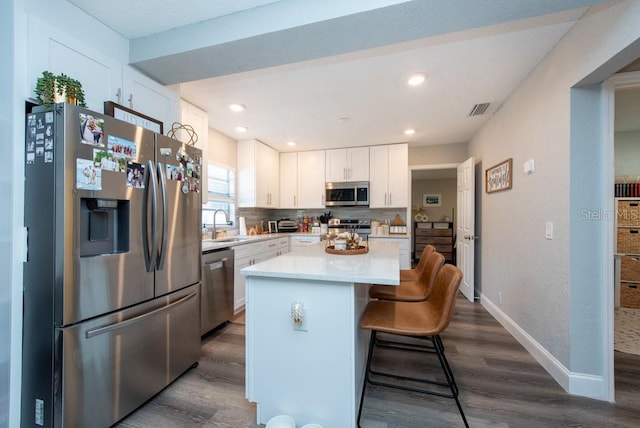 kitchen with appliances with stainless steel finishes, a center island, white cabinetry, dark wood-type flooring, and a breakfast bar area