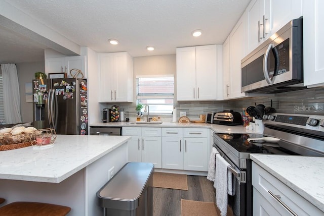 kitchen with white cabinetry, appliances with stainless steel finishes, sink, and a kitchen bar