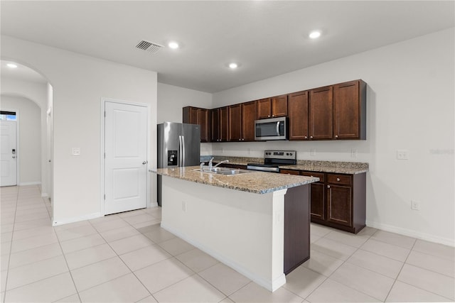 kitchen featuring sink, an island with sink, stainless steel appliances, light stone counters, and light tile patterned floors