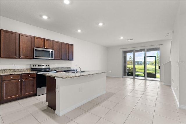 kitchen featuring light stone countertops, sink, light tile patterned flooring, stainless steel appliances, and a kitchen island with sink