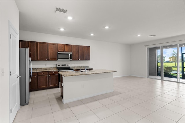 kitchen with a kitchen island with sink, sink, light tile patterned floors, appliances with stainless steel finishes, and light stone counters