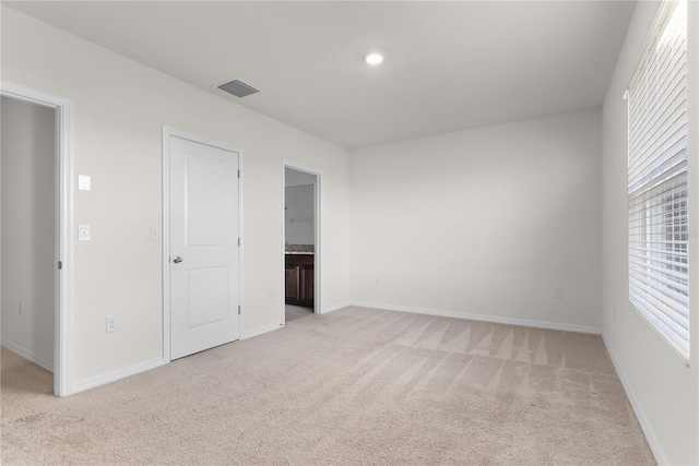 unfurnished bedroom with connected bathroom, multiple windows, and light colored carpet