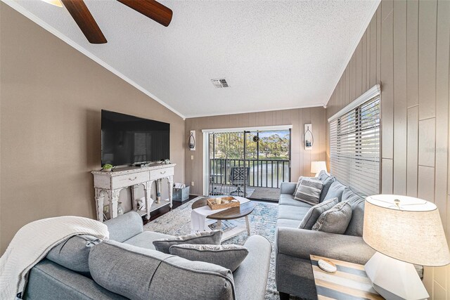 living room featuring ceiling fan, ornamental molding, lofted ceiling, and wooden walls