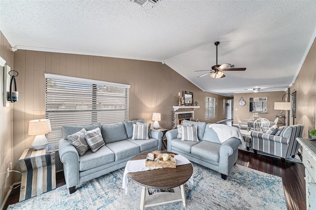 living room with ornamental molding, vaulted ceiling, dark hardwood / wood-style flooring, a textured ceiling, and ceiling fan