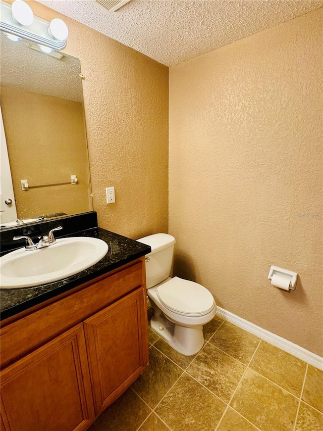 bathroom featuring vanity, toilet, tile patterned floors, and a textured ceiling