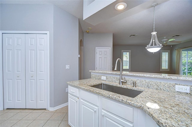 kitchen with light stone countertops, sink, pendant lighting, white cabinets, and light tile patterned floors