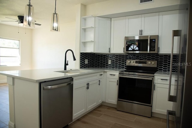 kitchen featuring hanging light fixtures, kitchen peninsula, sink, white cabinetry, and appliances with stainless steel finishes