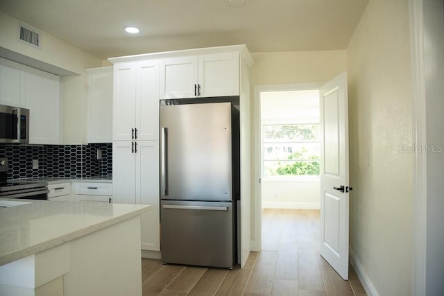 kitchen with light stone countertops, light wood-type flooring, white cabinetry, appliances with stainless steel finishes, and tasteful backsplash