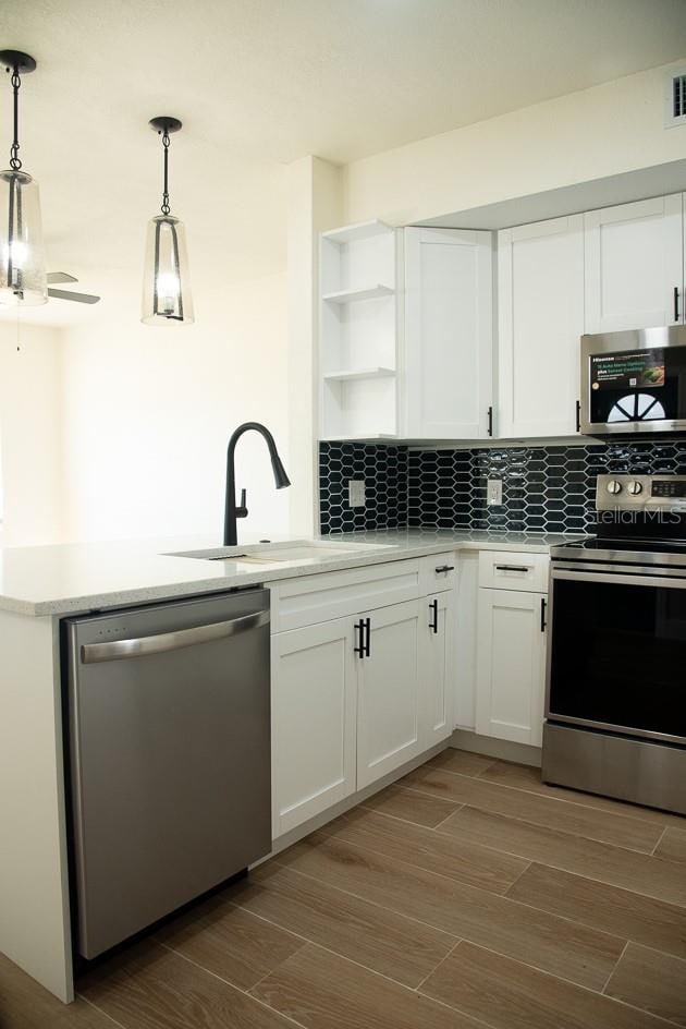 kitchen with white cabinetry, stainless steel appliances, decorative light fixtures, and sink