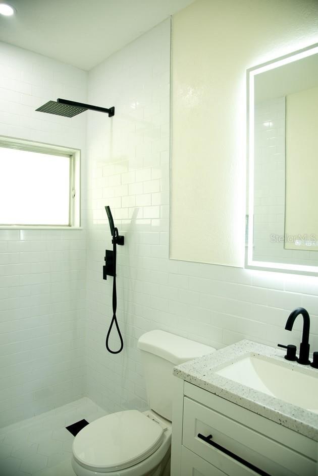 bathroom featuring tasteful backsplash, tile walls, toilet, tiled shower, and vanity