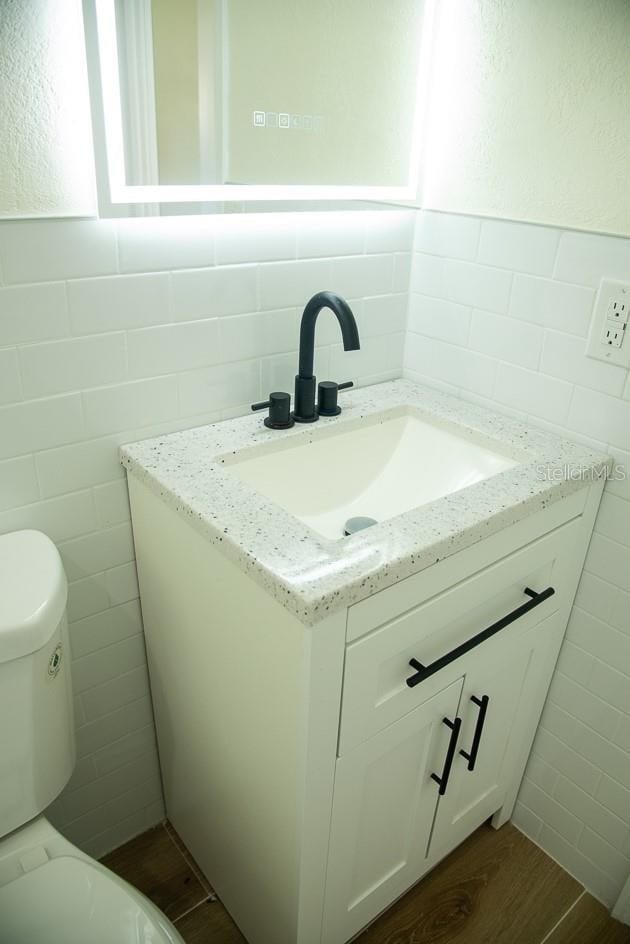 bathroom with toilet, hardwood / wood-style flooring, vanity, and tile walls