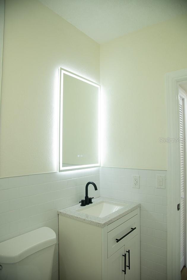 bathroom with vanity, toilet, and tile walls