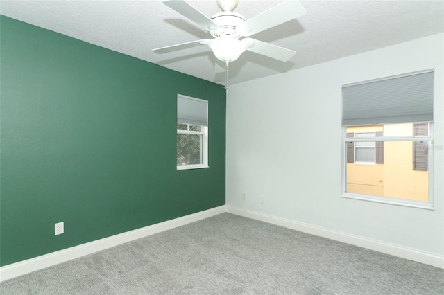 carpeted spare room featuring a textured ceiling, ceiling fan, and a healthy amount of sunlight