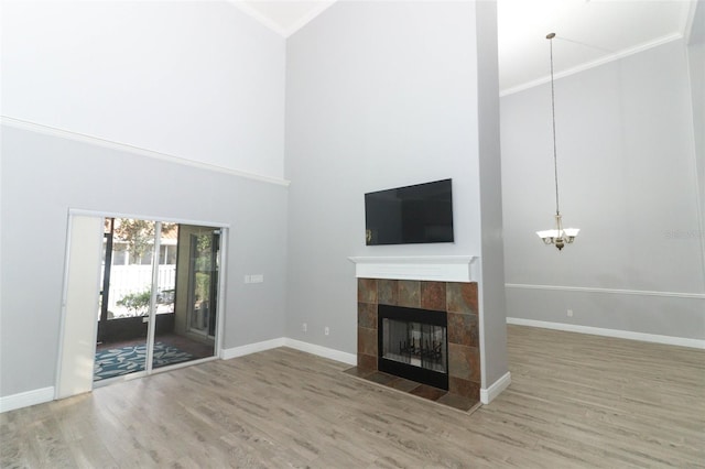 unfurnished living room featuring hardwood / wood-style floors, ornamental molding, a towering ceiling, and a tiled fireplace