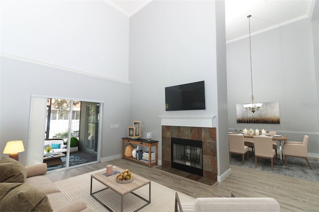 living room with a notable chandelier, crown molding, light wood-type flooring, a tiled fireplace, and high vaulted ceiling