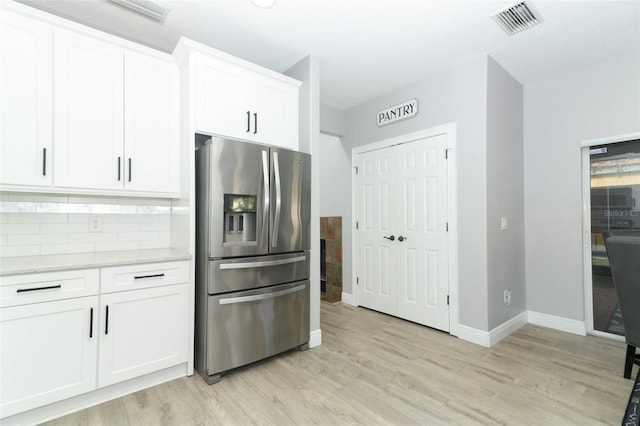 kitchen featuring light hardwood / wood-style floors, stainless steel fridge, tasteful backsplash, white cabinets, and light stone counters