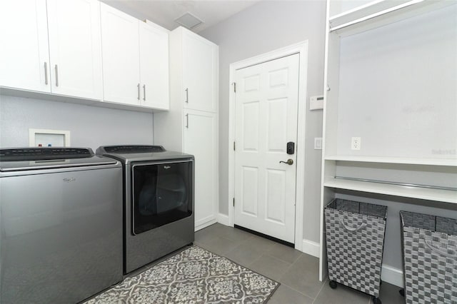 laundry room with dark tile patterned floors, washer and dryer, and cabinets