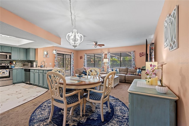 dining room with light carpet, sink, and ceiling fan with notable chandelier