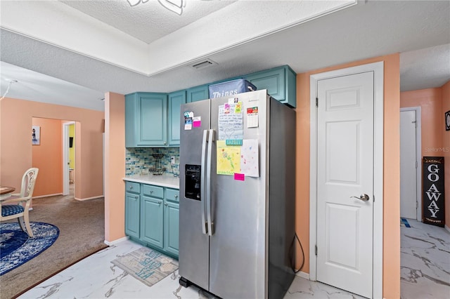 kitchen featuring stainless steel fridge, tasteful backsplash, a textured ceiling, blue cabinetry, and light colored carpet