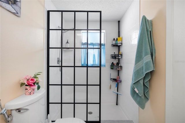 bathroom featuring toilet, a textured ceiling, and tiled shower