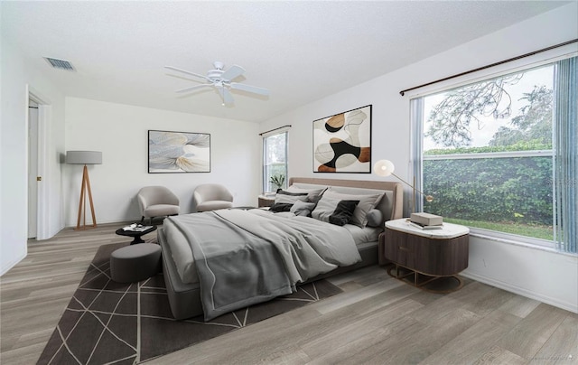 bedroom with ceiling fan, hardwood / wood-style floors, multiple windows, and a textured ceiling