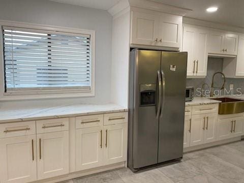 kitchen featuring white cabinets, sink, light stone counters, and stainless steel fridge with ice dispenser