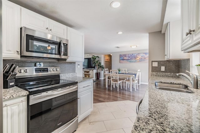 kitchen with stainless steel appliances, light stone countertops, sink, and white cabinets