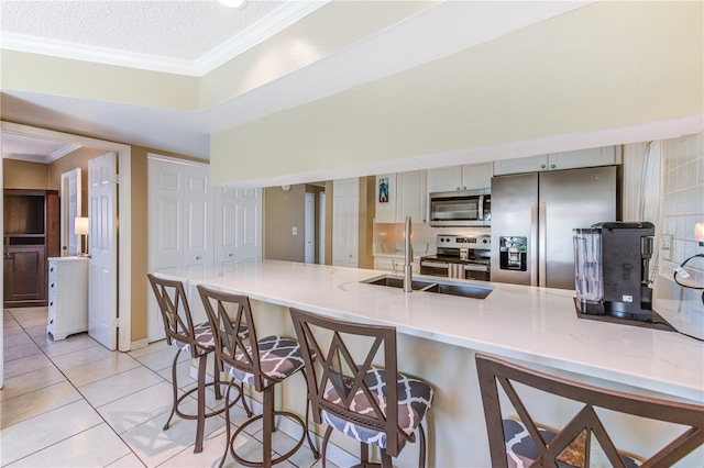 kitchen featuring kitchen peninsula, light tile patterned floors, appliances with stainless steel finishes, a breakfast bar area, and sink