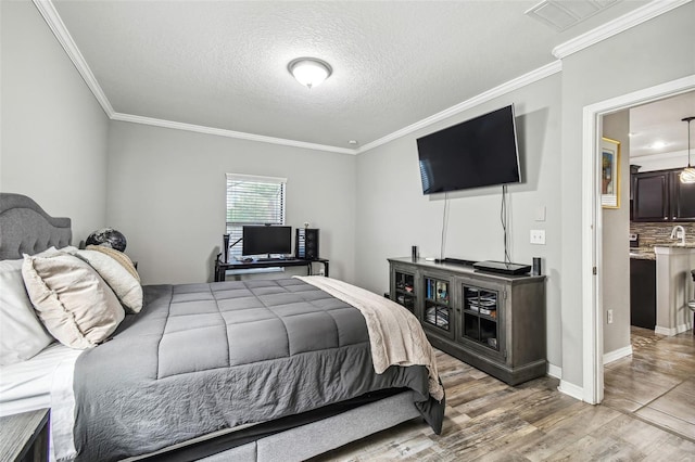 bedroom featuring sink, wood-type flooring, a textured ceiling, and ornamental molding