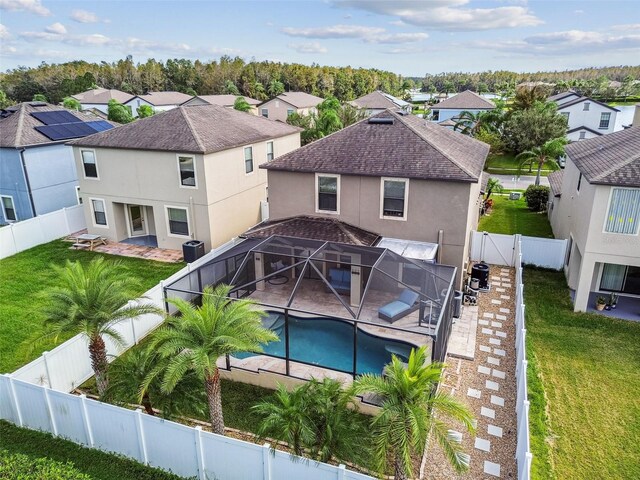 back of property featuring glass enclosure, a yard, a fenced in pool, a patio area, and central air condition unit