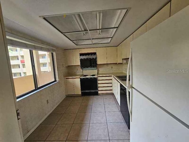 kitchen with sink, black appliances, cream cabinetry, and light tile patterned floors