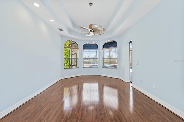 empty room featuring a raised ceiling, ceiling fan, and wood-type flooring