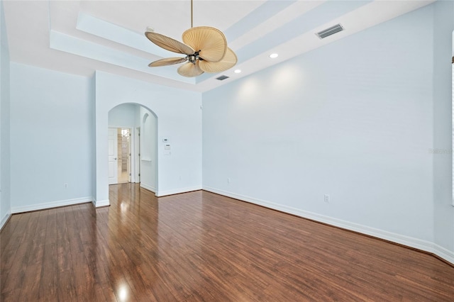 unfurnished room featuring a raised ceiling, ceiling fan, and dark hardwood / wood-style flooring