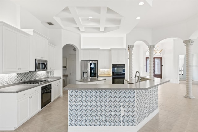 kitchen featuring white cabinets, ornate columns, stainless steel appliances, and a large island with sink