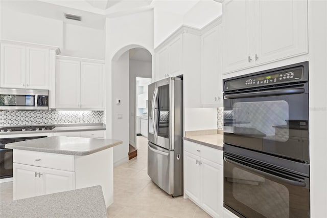 kitchen with appliances with stainless steel finishes, backsplash, light tile patterned floors, white cabinetry, and a kitchen island