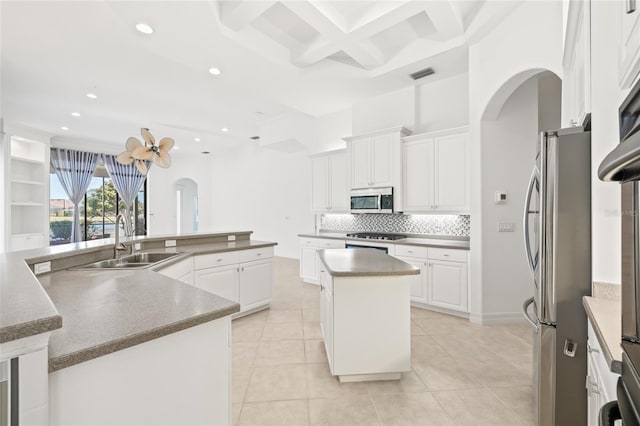 kitchen with white cabinets, sink, appliances with stainless steel finishes, beamed ceiling, and a kitchen island