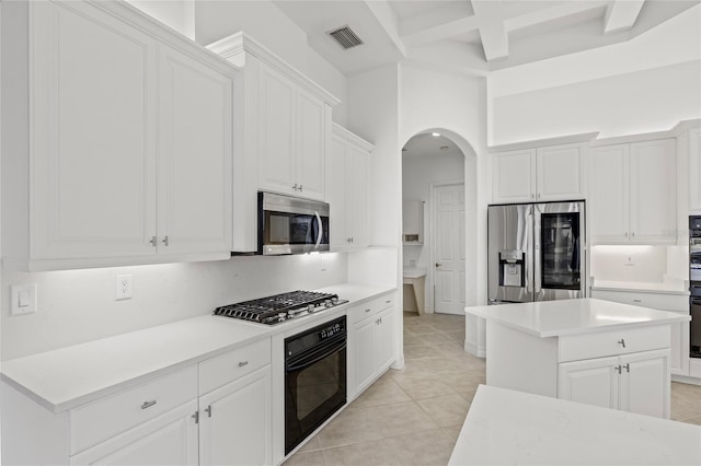 kitchen featuring appliances with stainless steel finishes, a towering ceiling, beamed ceiling, white cabinets, and a center island