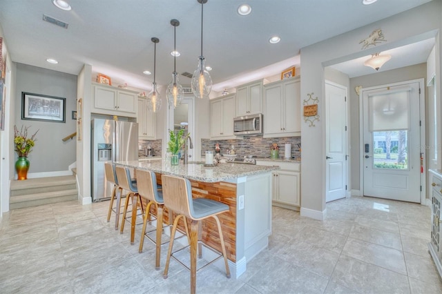 kitchen featuring a kitchen bar, appliances with stainless steel finishes, tasteful backsplash, a kitchen island with sink, and pendant lighting