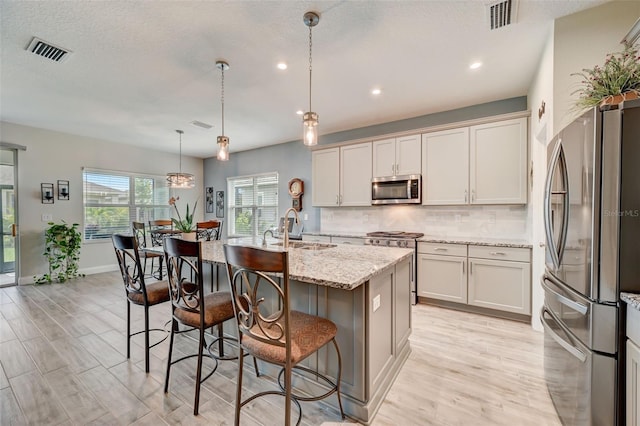 kitchen featuring decorative light fixtures, a center island with sink, sink, light stone countertops, and appliances with stainless steel finishes