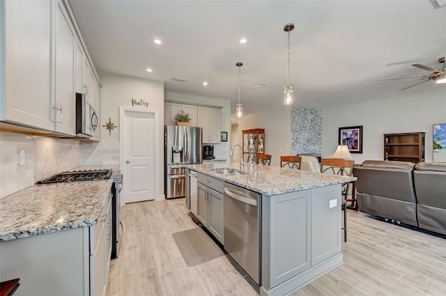 kitchen featuring decorative light fixtures, sink, a kitchen island with sink, light wood-type flooring, and stainless steel appliances