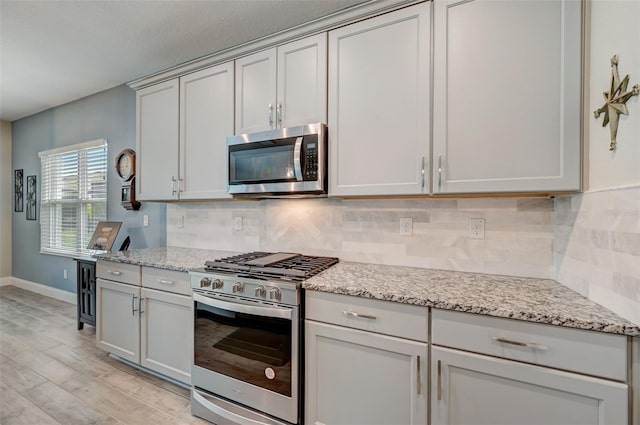 kitchen featuring appliances with stainless steel finishes, light hardwood / wood-style floors, tasteful backsplash, and light stone countertops