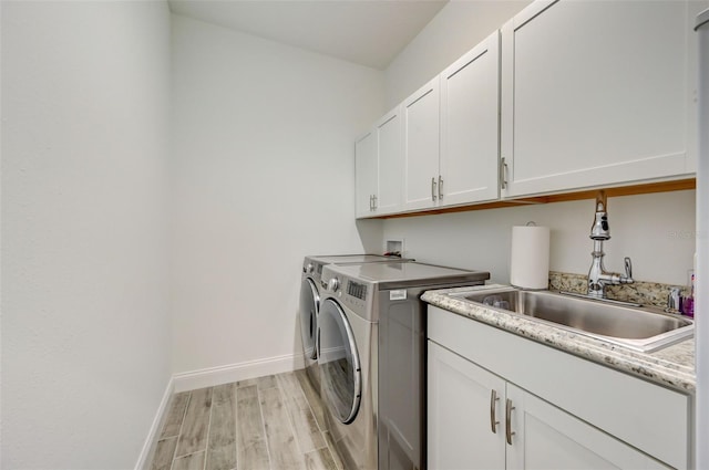 washroom with light wood-type flooring, sink, separate washer and dryer, and cabinets