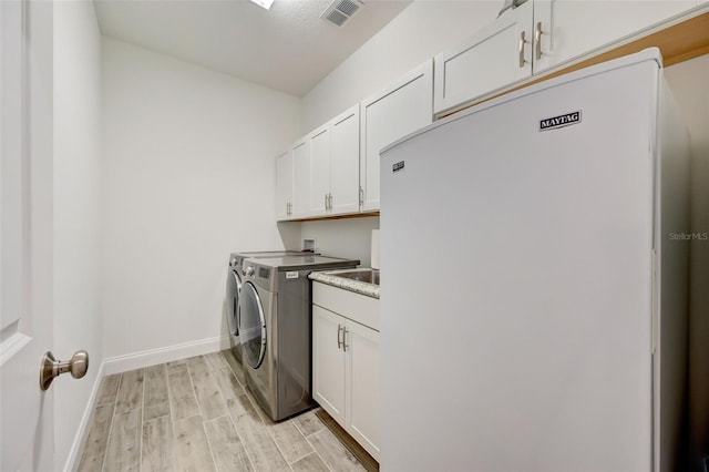 washroom with light wood-type flooring, separate washer and dryer, and cabinets