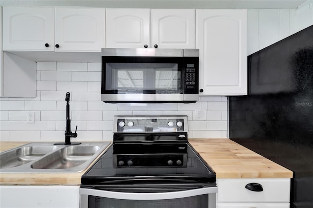 kitchen with butcher block counters, sink, black appliances, white cabinets, and tasteful backsplash