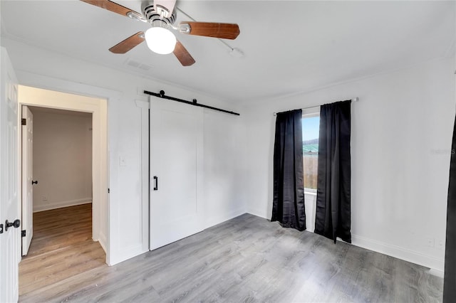 spare room featuring ceiling fan, light wood-type flooring, and a barn door