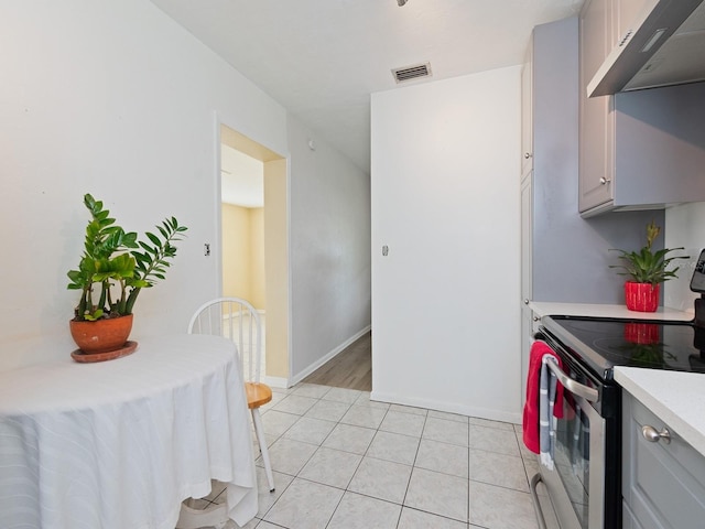 kitchen with gray cabinets, light tile patterned flooring, stainless steel electric range, and exhaust hood