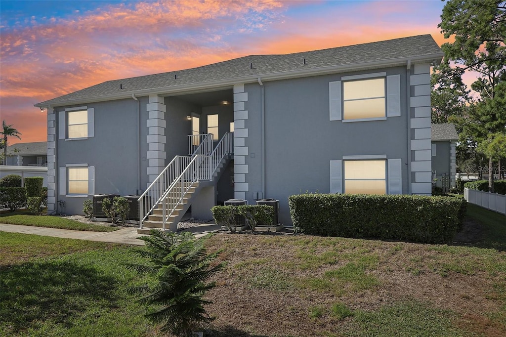 townhome / multi-family property with a lawn, stairway, stucco siding, and roof with shingles